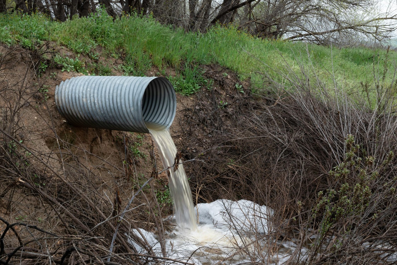 A rural drainage pipe pouring water into a natural ravine, surrounded by green vegetation.