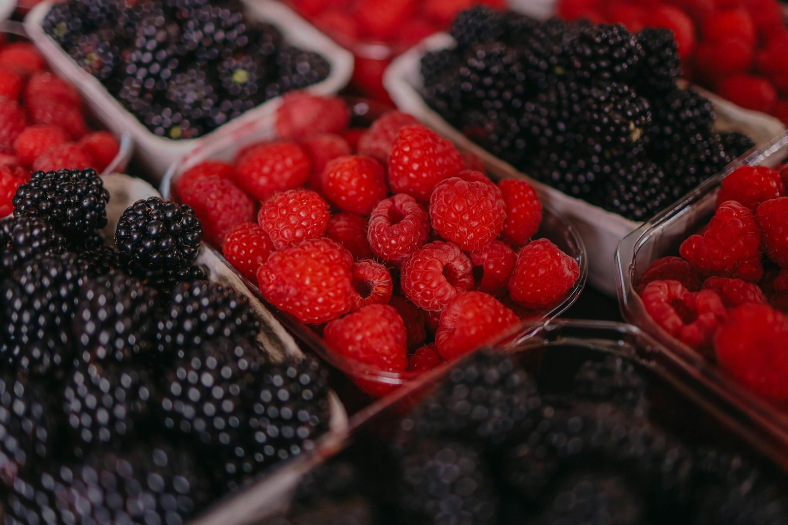 A vibrant close-up of fresh blackberries and raspberries displayed in baskets at a market.