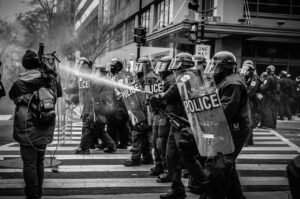 people, police, protest, water, shield, helmet, gear, nature, pedestrian, camera, reporter, black and white, gray water, gray police, gray camera